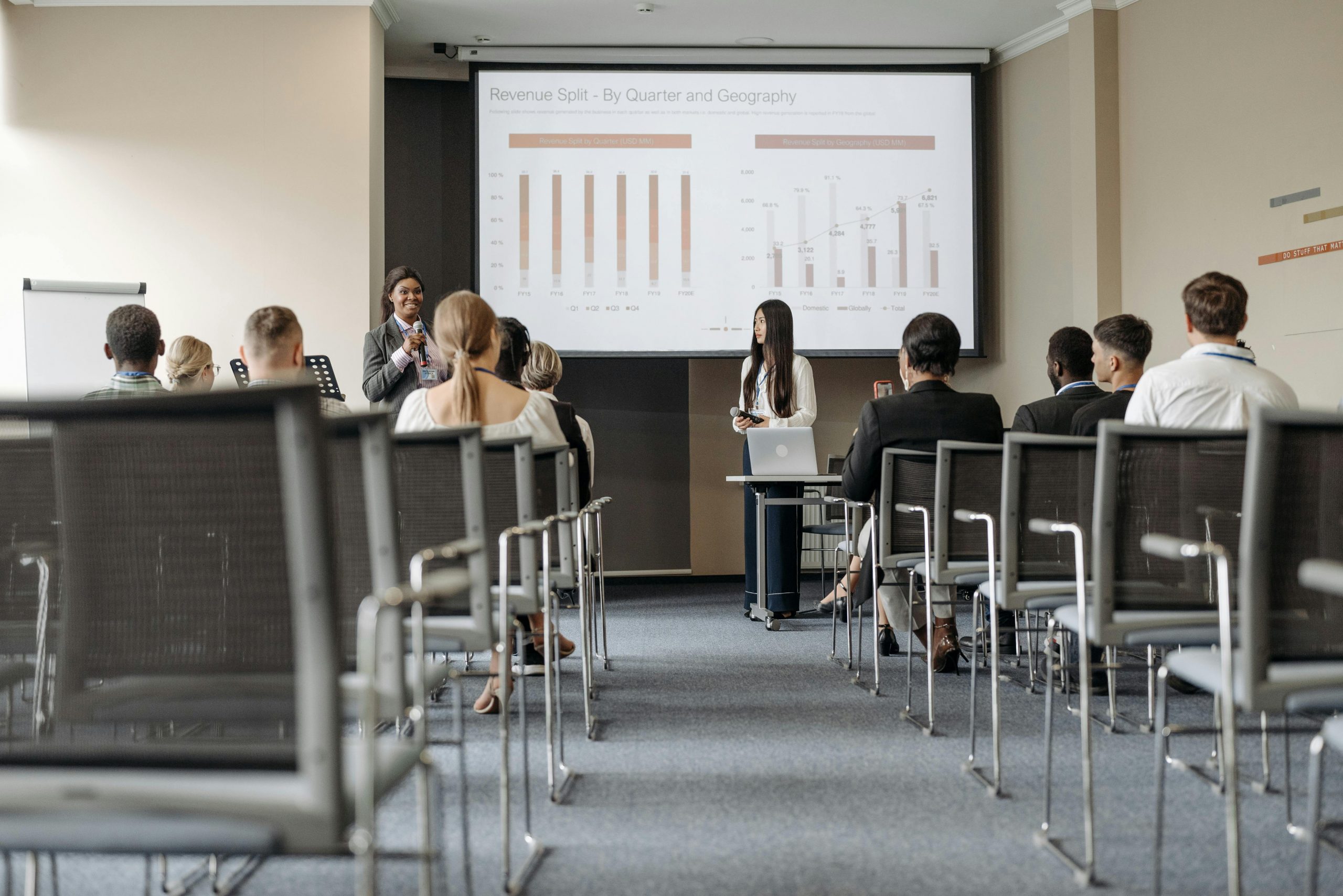 Business conference attendees listen to a presentation on revenue split by quarter and geography.